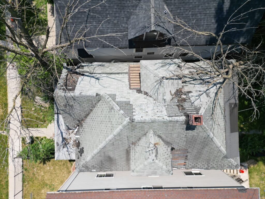 Close-up of an old roof with faded, curling shingles and visible damage from years of wear and weather exposure.