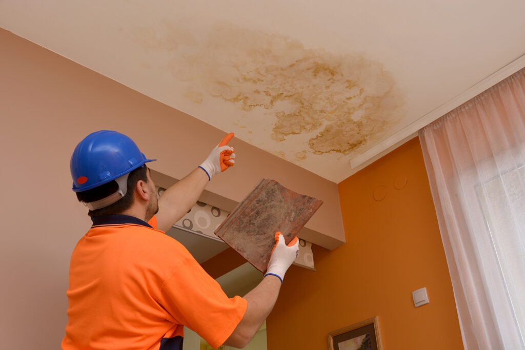 Water leaking from a damaged roof, dripping onto the ceiling and leaving visible stains.